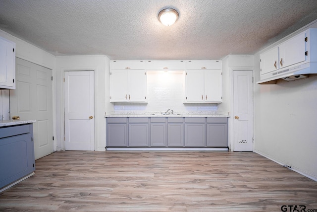 kitchen featuring a textured ceiling, light hardwood / wood-style floors, and white cabinetry