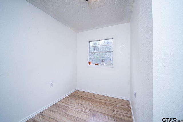 spare room featuring light wood-type flooring, a textured ceiling, and vaulted ceiling