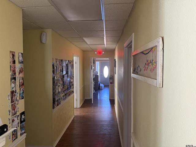 hall with a paneled ceiling, wood-type flooring, and baseboards