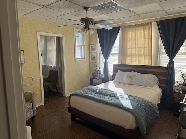 bedroom with ceiling fan, a drop ceiling, wood finished floors, and visible vents