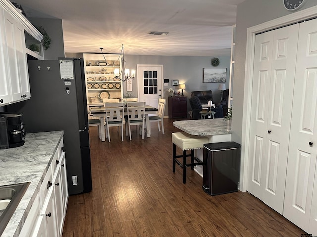 kitchen featuring a chandelier, light stone counters, dark wood-style flooring, white cabinetry, and pendant lighting