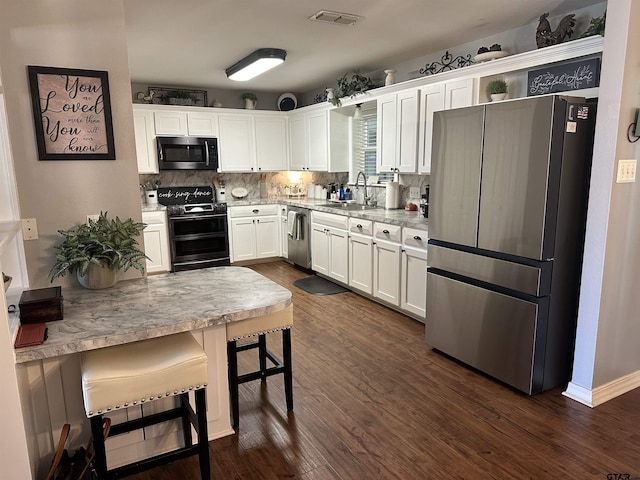 kitchen with dark wood-style floors, tasteful backsplash, appliances with stainless steel finishes, white cabinetry, and a sink