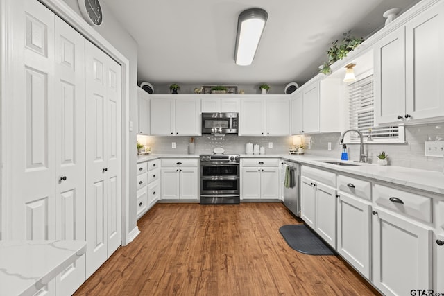 5513 Bostick Dr, Tyler, TX 75707 - kitchen with stainless steel appliances, a sink, white cabinetry, decorative backsplash, and wood finished floors