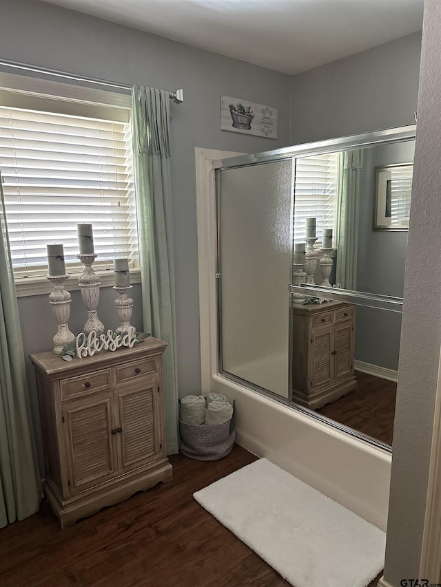 bathroom featuring enclosed tub / shower combo, a healthy amount of sunlight, and wood finished floors