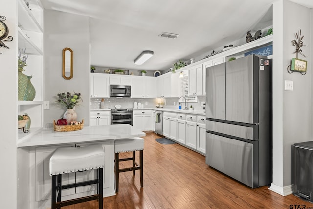 5513 Bostick Dr, Tyler, TX 75707 - kitchen with stainless steel appliances, white cabinetry, wood finished floors, a kitchen bar, and a peninsula