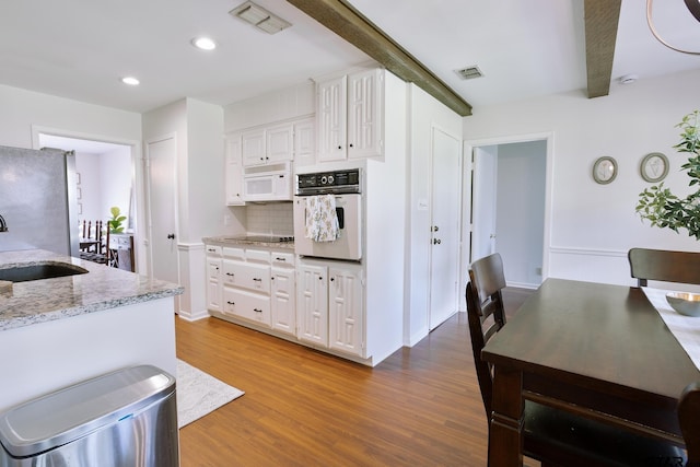 813 W Rieck Rd, Tyler, TX 75703 - kitchen featuring white appliances, wood finished floors, white cabinets, light stone countertops, and tasteful backsplash