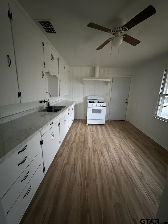 kitchen with white cabinets, sink, light stone countertops, light hardwood / wood-style floors, and white range with gas cooktop