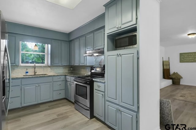 150 Gambrell St, Rusk, TX 75785 - kitchen featuring appliances with stainless steel finishes, under cabinet range hood, tasteful backsplash, light wood-style floors, and light stone counters