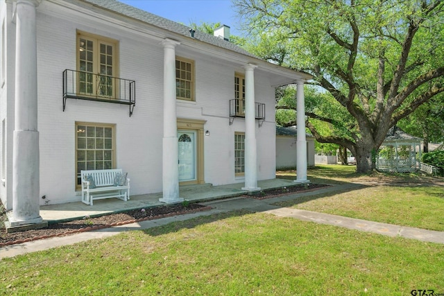 greek revival inspired property featuring a chimney, a front lawn, brick siding, and a balcony