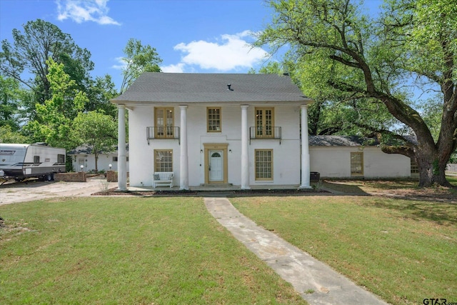 neoclassical home with stucco siding, a balcony, a shingled roof, and a front yard