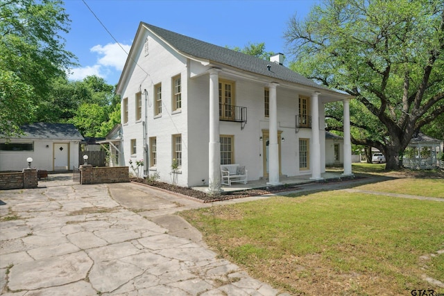 view of front of property with an outbuilding, a front lawn, a chimney, a balcony, and a patio