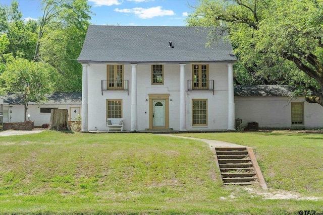 view of front of home featuring brick siding, a shingled roof, a front lawn, and a balcony