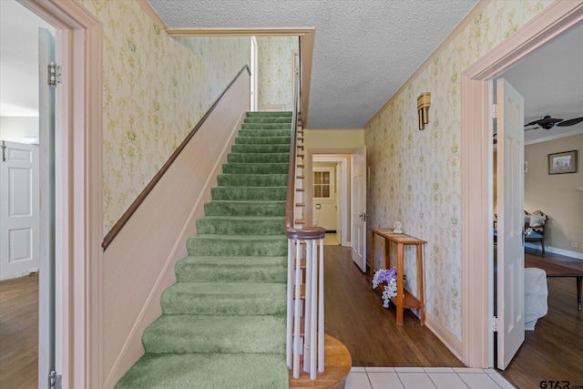 stairs with baseboards, wood finished floors, wallpapered walls, and a textured ceiling
