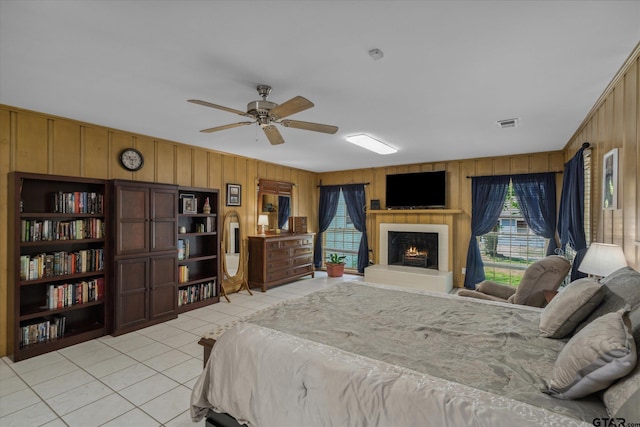 bedroom with a warm lit fireplace, wood walls, light tile patterned flooring, and multiple windows