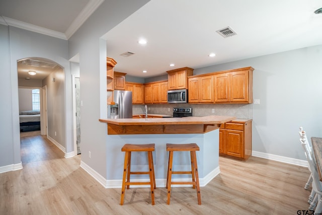 kitchen with sink, a breakfast bar area, stainless steel appliances, light hardwood / wood-style floors, and backsplash