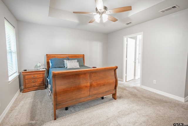 carpeted bedroom with a raised ceiling and ceiling fan