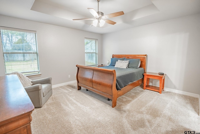 bedroom with ceiling fan, light colored carpet, and a tray ceiling