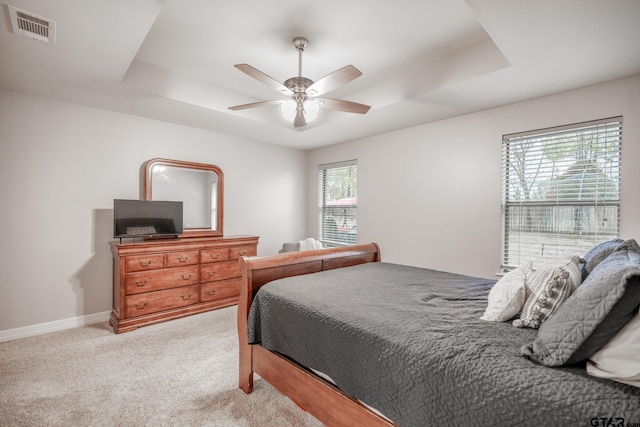 carpeted bedroom with ceiling fan and a tray ceiling