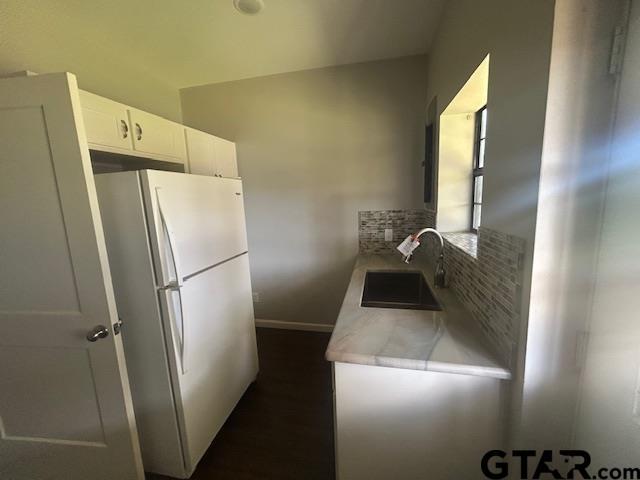 kitchen with a sink, light countertops, freestanding refrigerator, white cabinetry, and baseboards