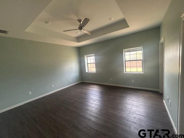 spare room with a raised ceiling, ceiling fan, dark wood finished floors, and visible vents