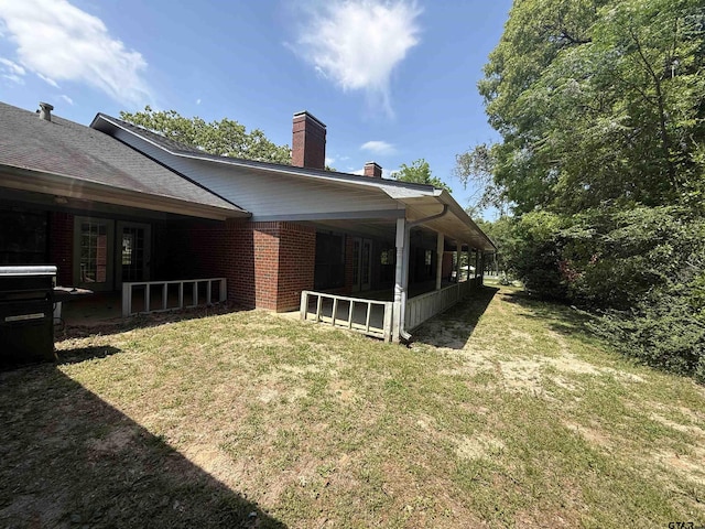 back of house with a chimney, brick siding, and a yard