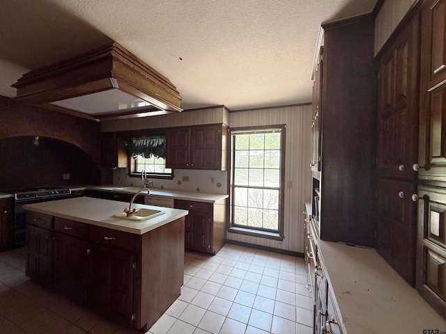 kitchen with a sink, electric range, light countertops, an island with sink, and light tile patterned floors