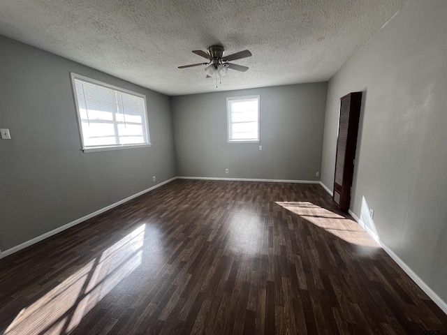 unfurnished room with a textured ceiling, baseboards, dark wood finished floors, and a ceiling fan