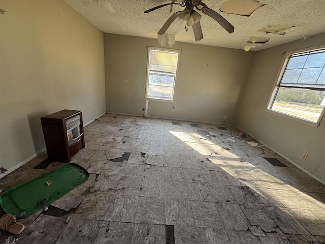 spare room featuring a healthy amount of sunlight, a wood stove, a textured ceiling, and a ceiling fan