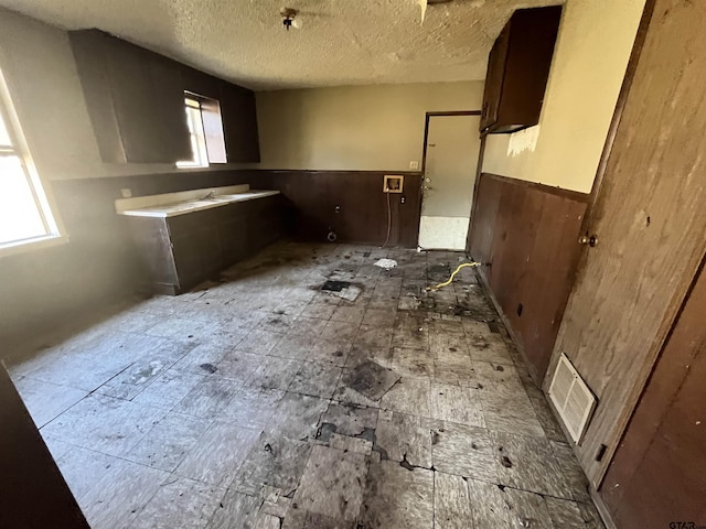 kitchen featuring wainscoting, wood walls, visible vents, and a textured ceiling