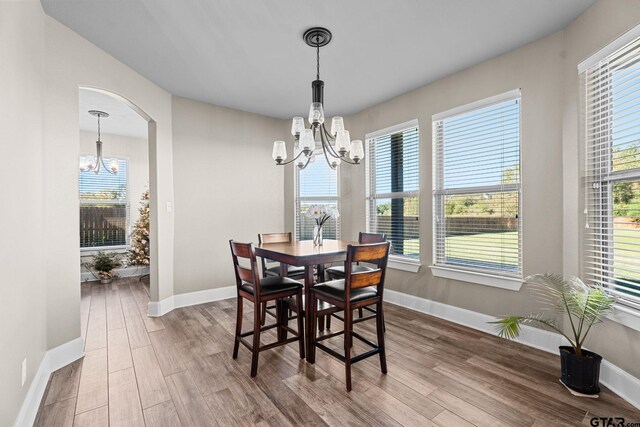 dining area with an inviting chandelier, wood finished floors, and arched walkways