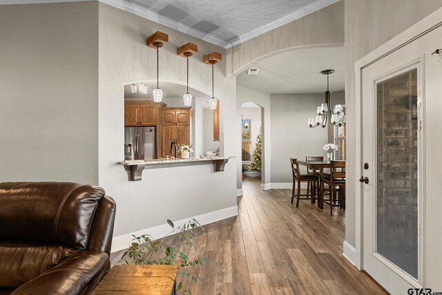 interior space with stainless steel refrigerator with ice dispenser, a kitchen breakfast bar, arched walkways, brown cabinetry, and dark wood-style flooring