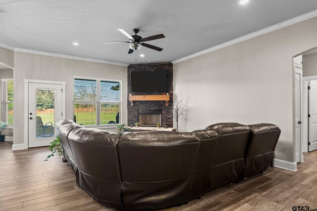 living room featuring a stone fireplace, crown molding, a ceiling fan, and wood finished floors