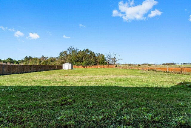 view of yard with a rural view, a storage unit, a fenced backyard, and an outdoor structure