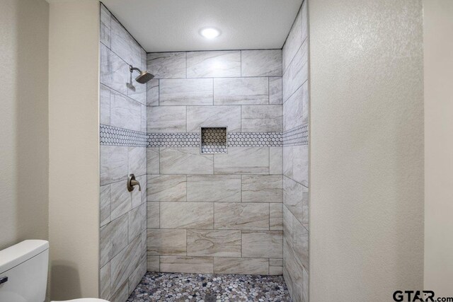 bathroom featuring toilet, tiled shower, and recessed lighting