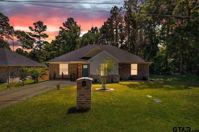view of front of house featuring concrete driveway, brick siding, and a lawn