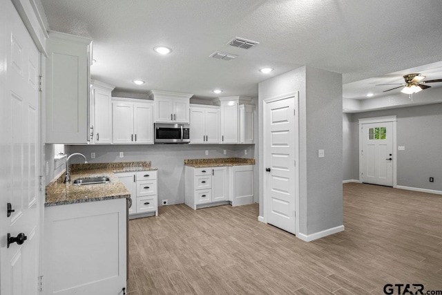 kitchen featuring stainless steel microwave, a sink, dark stone countertops, and visible vents