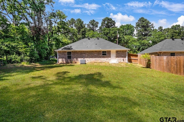 back of property with central AC unit, fence, brick siding, and a lawn