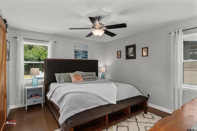 bedroom with dark hardwood / wood-style floors, ceiling fan, and a barn door