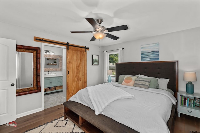 bedroom featuring sink, dark hardwood / wood-style flooring, ceiling fan, a barn door, and ensuite bath