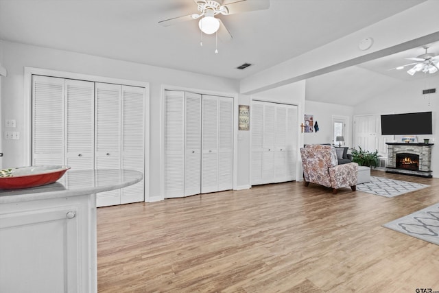 living room featuring ceiling fan, a fireplace, vaulted ceiling, light hardwood / wood-style flooring, and sink