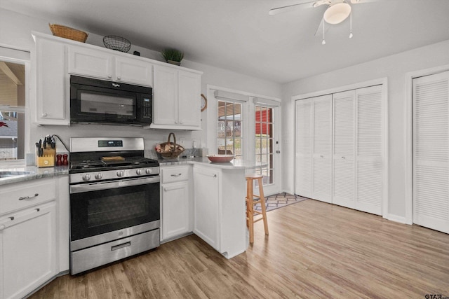 kitchen featuring ceiling fan, kitchen peninsula, stainless steel range with gas cooktop, white cabinetry, and light wood-type flooring