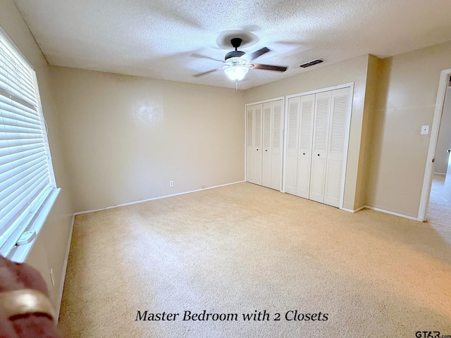 3900 S Donnybrook Ave, Tyler, TX 75703 - unfurnished bedroom featuring carpet flooring, two closets, baseboards, a textured ceiling, and a ceiling fan