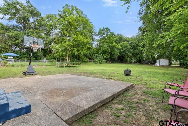 1135 E Sixth St, Tyler, TX 75701 - fenced backyard with a trampoline, a shed, an outdoor fire pit, a patio, and view of wooded area