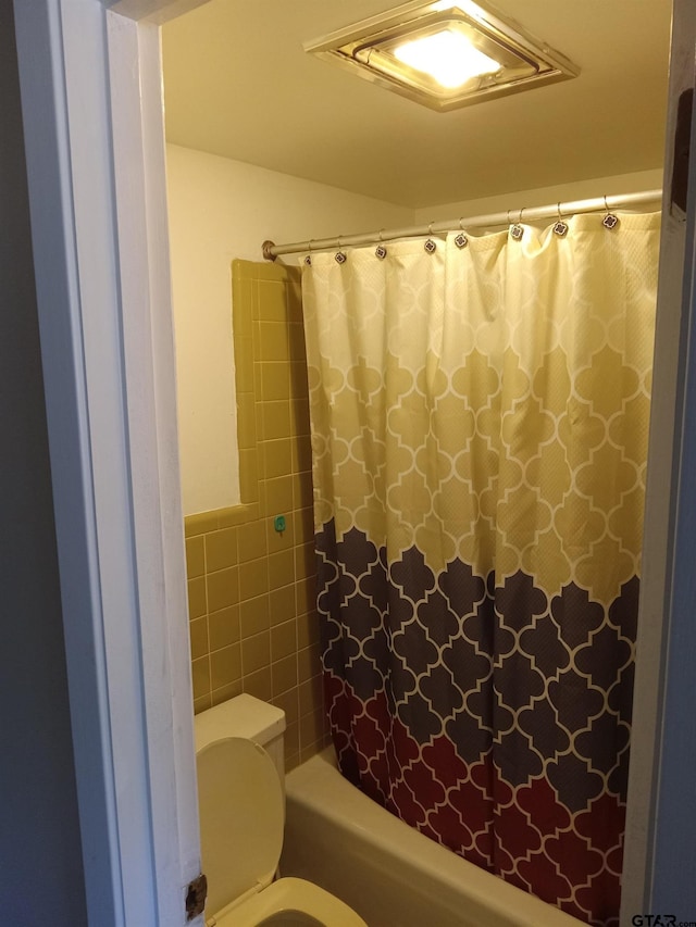 bathroom featuring tile walls, toilet, and shower / bathtub combination with curtain