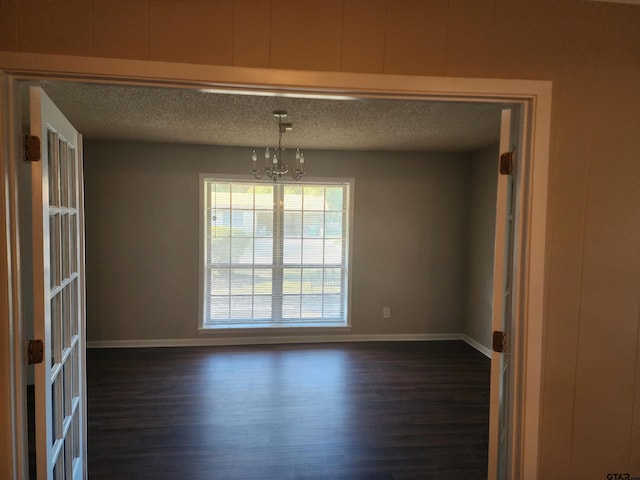 unfurnished dining area with dark hardwood / wood-style floors, a textured ceiling, and a chandelier