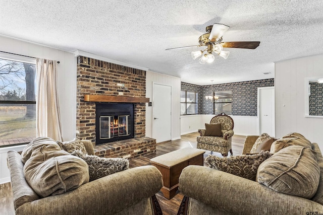 living room with ceiling fan, hardwood / wood-style floors, a brick fireplace, and a textured ceiling