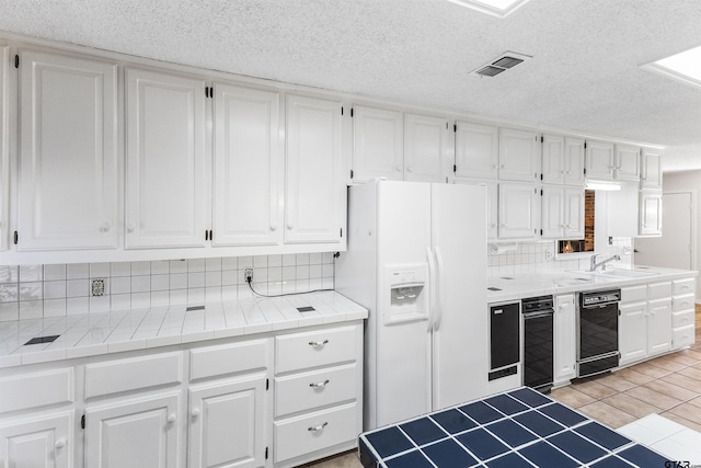 kitchen featuring white cabinetry, white refrigerator with ice dispenser, sink, and tile counters