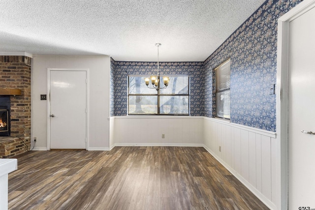 unfurnished dining area with an inviting chandelier, dark hardwood / wood-style floors, a brick fireplace, and a textured ceiling