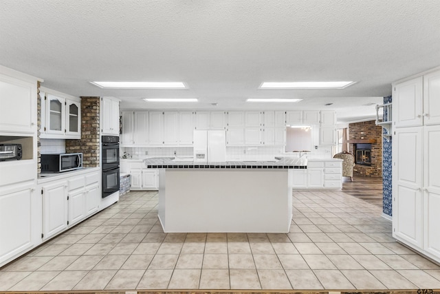 kitchen featuring double oven, white cabinetry, white refrigerator with ice dispenser, a center island, and light tile patterned floors