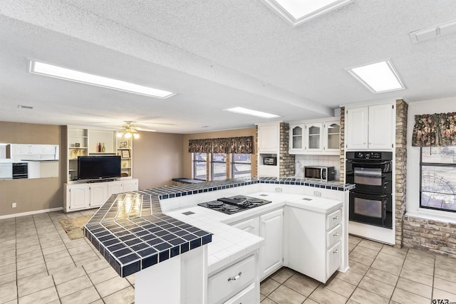 kitchen with white cabinetry, tile countertops, a kitchen island, and black appliances